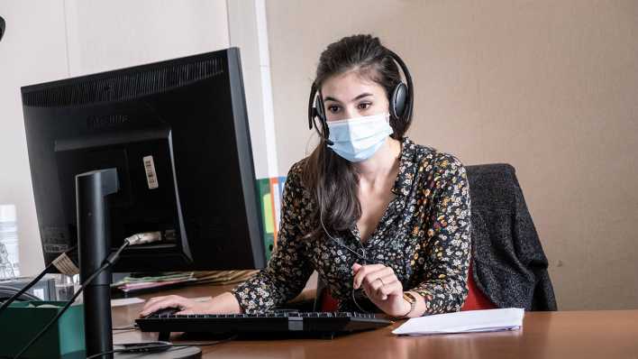 Eine junge Frau sitzt mit einer Maske am Telefon (Foto: imago images/Hans Lucas)