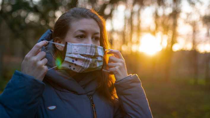 Eine junge Frau legt sich eine Mundschutzmaske an (Foto: imago images/Marius Schwarz)