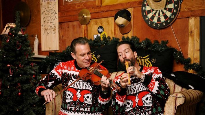 Alec und Sascha von The BossHoss in Weihnachtspullovern mit Flöte und Geige neben Weihnachtsbaum (Bild: rbb)