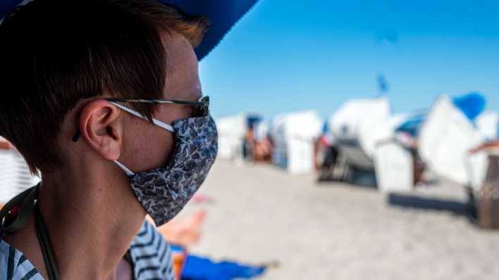 Eine Frau trägt eine Mund-Nasen-Maske am Strand von Grömitz; Quelle: David Inderlied/Kirchner-Media/www.imago-images.de